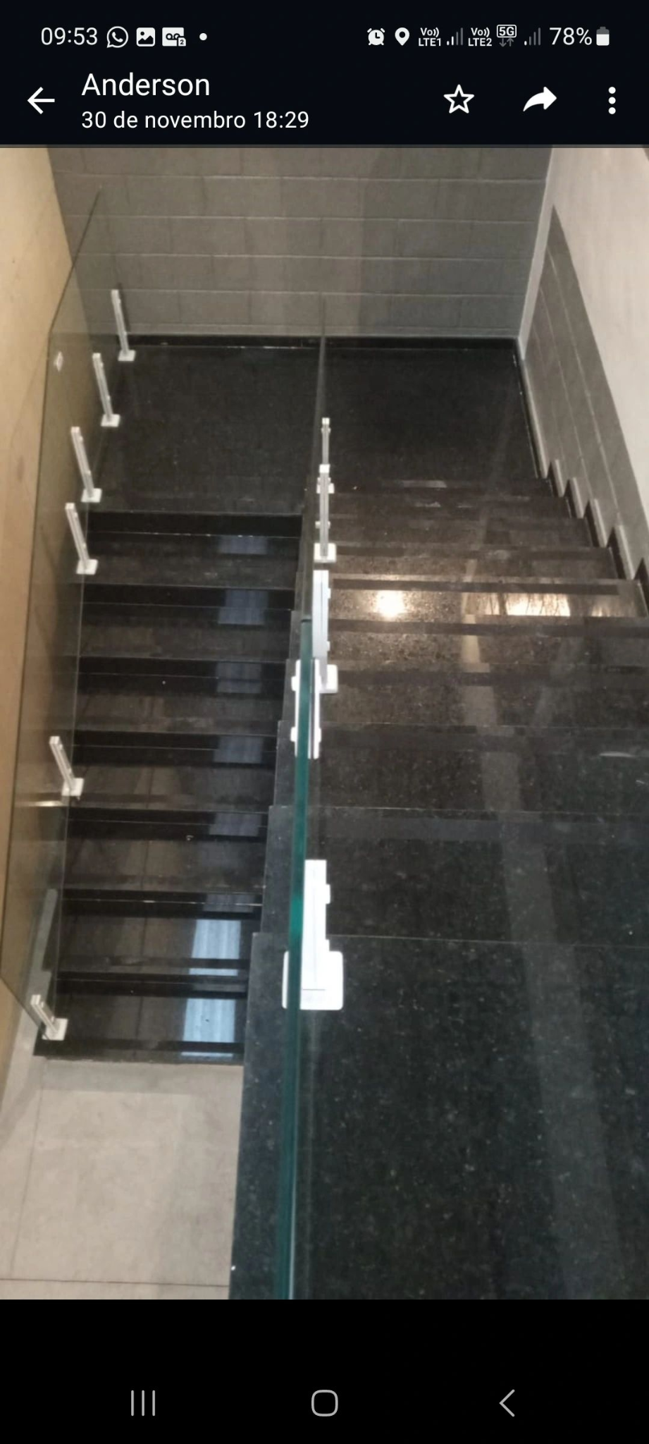 Escadaria interna com degraus escuros e guarda-corpo de vidro